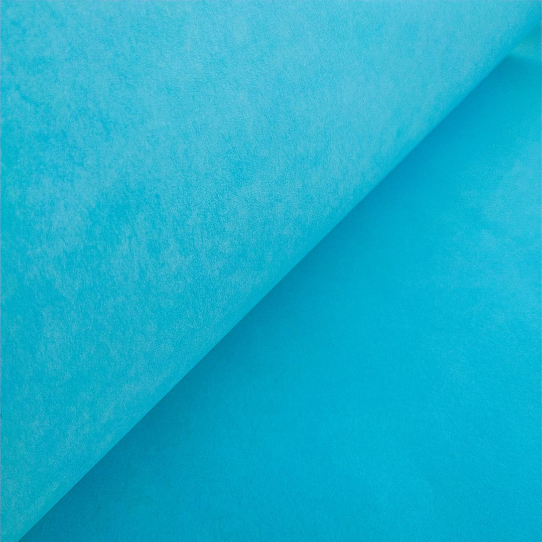 A close-up of Solid-Colored Kozo Paper (Atoll Blue) by Kozo Studio resembles delicate rice paper, with a partially unrolled sheet revealing a smooth, textured surface and creating a soft gradient of light and shadow.