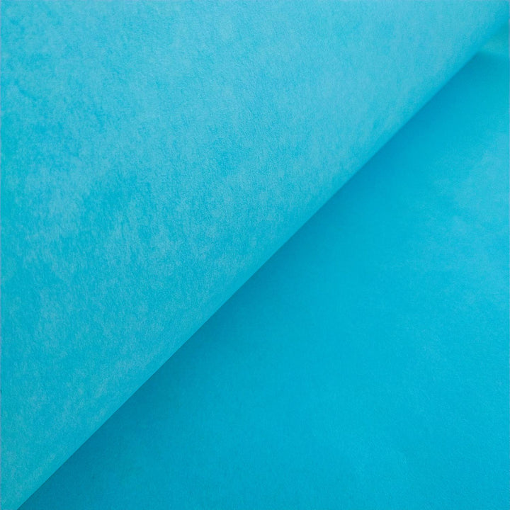 A close-up of Solid-Colored Kozo Paper (Atoll Blue) by Kozo Studio resembles delicate rice paper, with a partially unrolled sheet revealing a smooth, textured surface and creating a soft gradient of light and shadow.